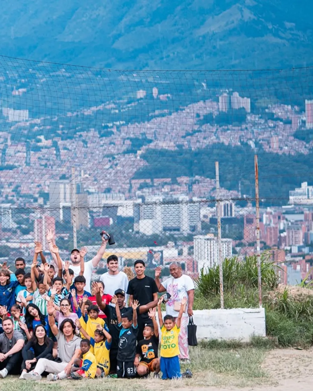Comunidad de 11 Cracks reunida en una cancha con Medellín de fondo, celebrando.
