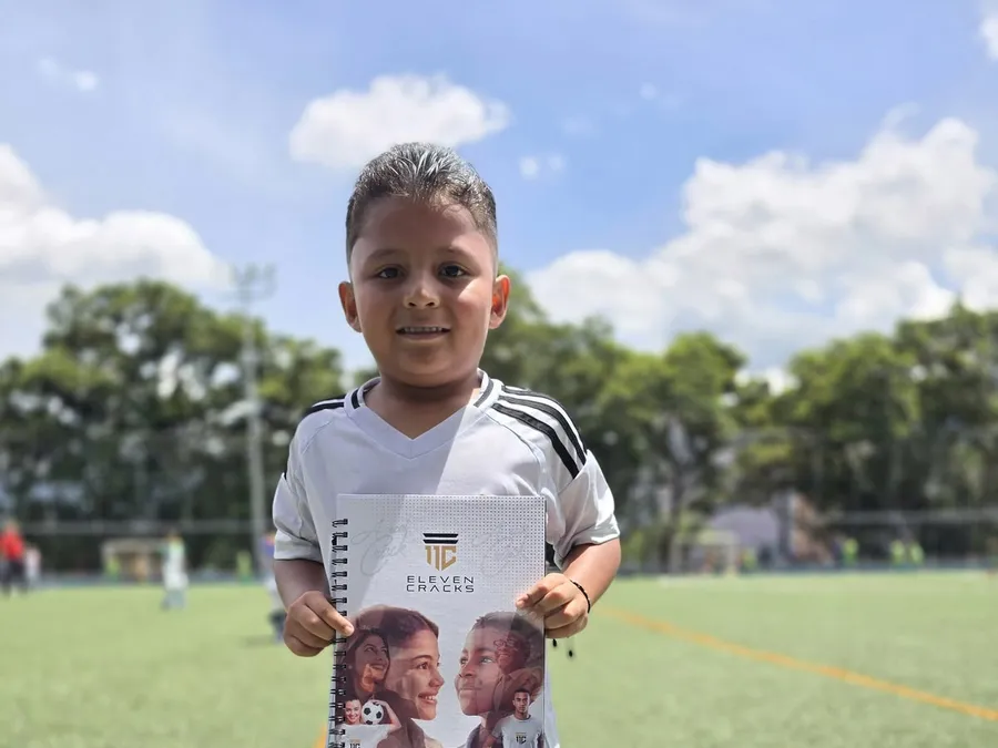 Un niño muestra su cuaderno de la Secretaría de Bilingüismo con el sello de 11 Cracks, en la cancha.