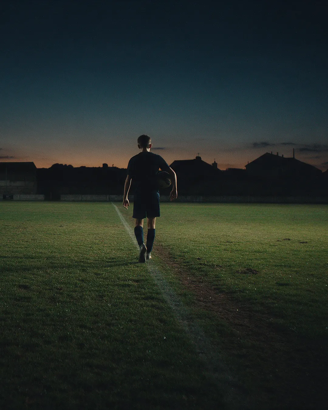 Un joven deportista camina hacia la cancha al atardecer.