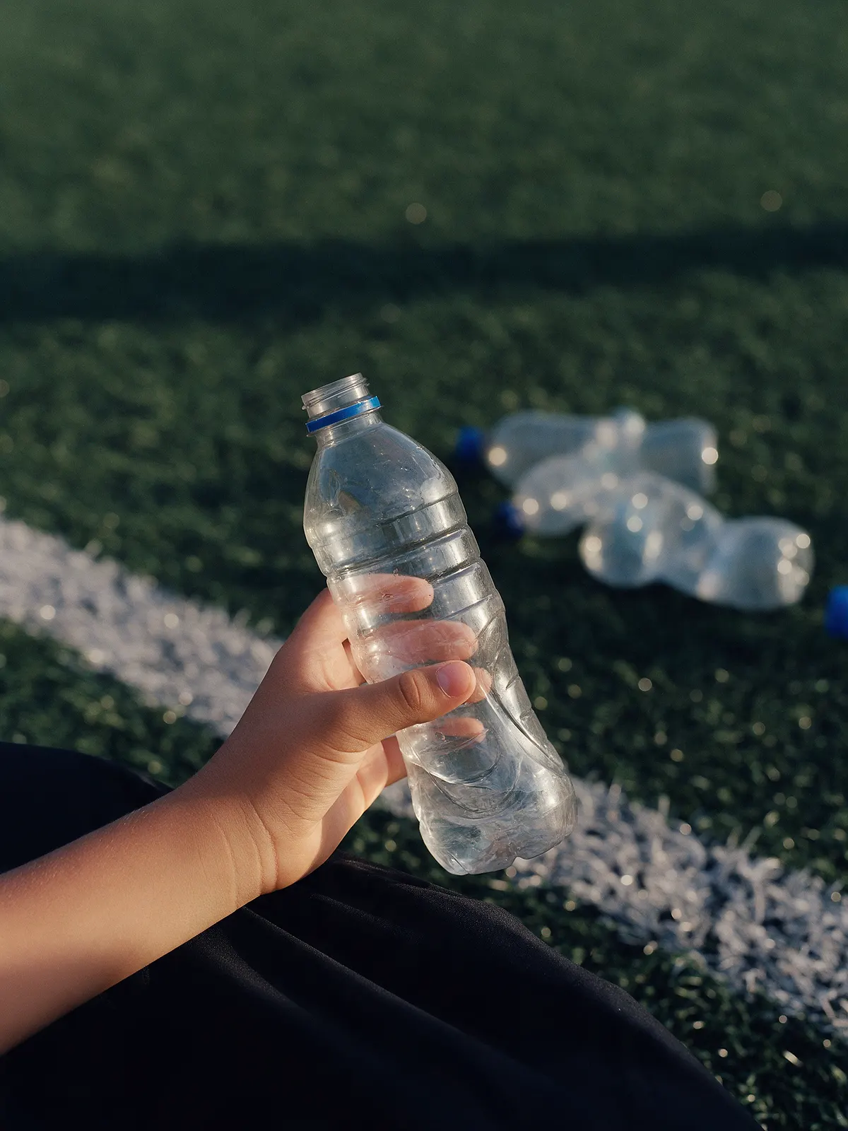 Una mano sostiene una botella PET transparente al borde de una cancha sintética.