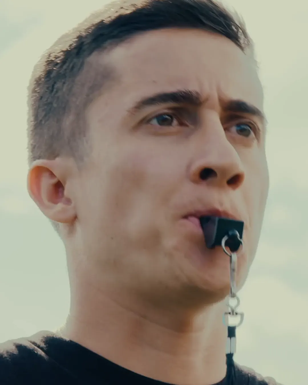 Un entrenador con silbato en los labios dirige la mirada al campo durante una sesión de entrenamiento.