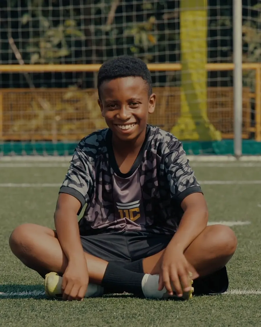 Un joven deportista sentado en el césped de la cancha, sonriendo.
