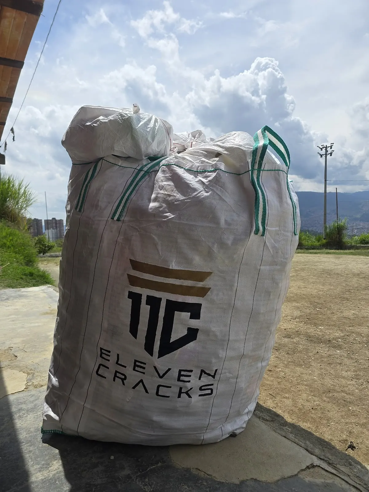 Costal de recolección de botellas PET con el logo de 11 Cracks, lleno, sobre una cancha.