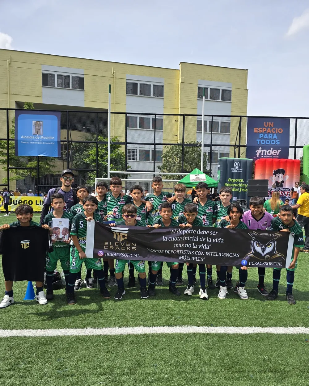 Equipo juvenil de 11 Cracks con el pendón del club en un torneo, junto a la Alcaldía de Medellín.