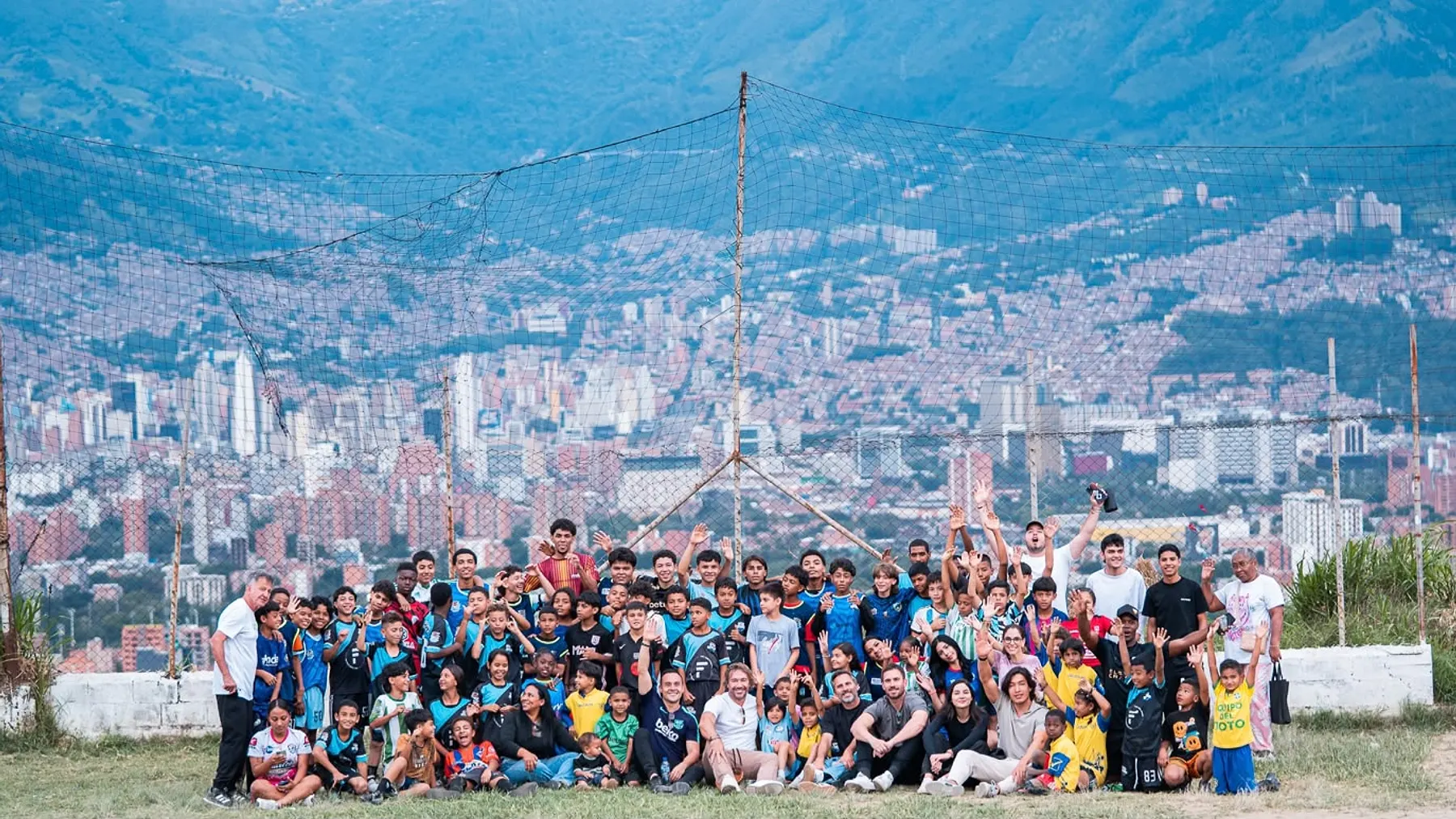 Un grupo numeroso de jóvenes y adultos de la comunidad, en una cancha de barrio con la ciudad de Medellín de fondo.